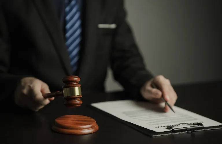 Person in a suit holding a wooden gavel near a legal document on a clipboard.