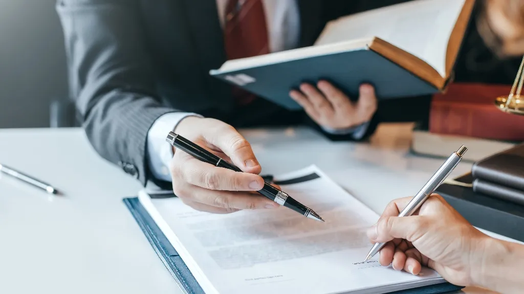 Two professionals reviewing and signing a document at a desk with legal books.