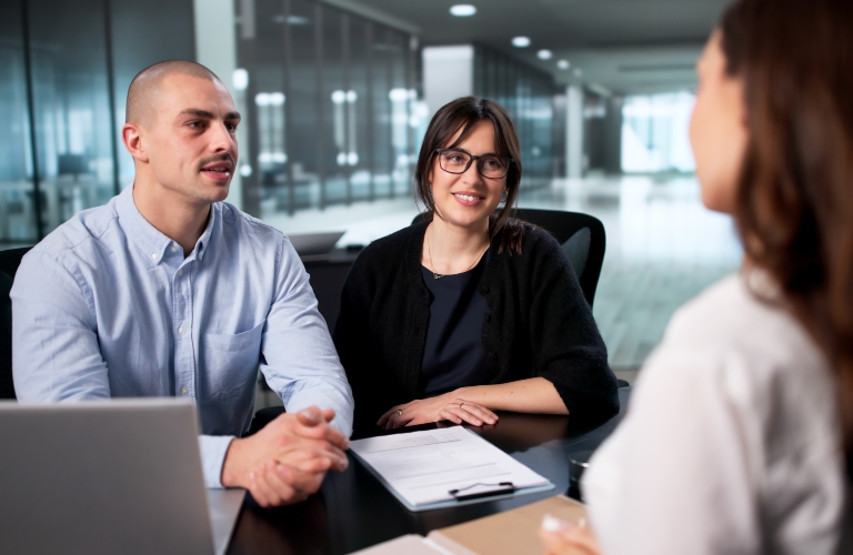 Three professionals engaged in a meeting at a modern office with documents and a laptop.