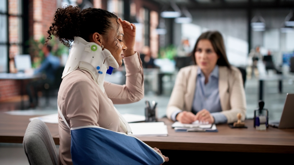 Injured woman with neck brace and arm sling consulting professional in modern office.