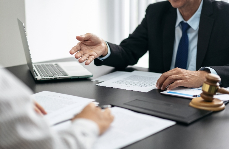 Two professionals discussing documents at a desk with a laptop and wooden gavel.