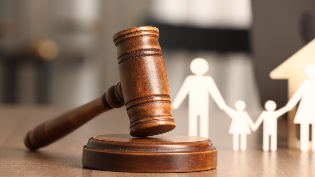 Wooden judge's gavel resting on a sound block with blurred paper cutout family figures.